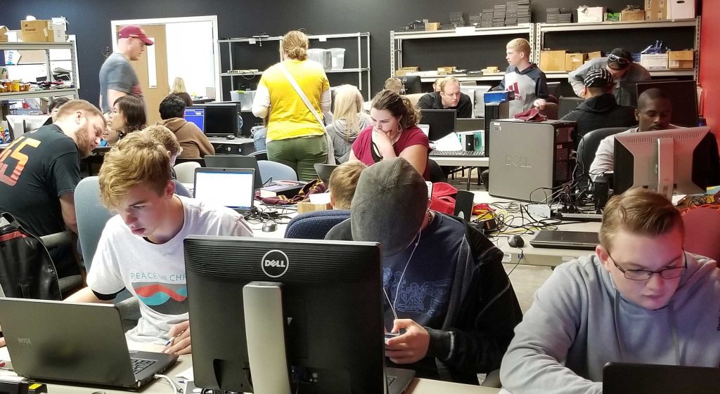 Picture of Computers for the Blind's workroom, with many volunteers working on computers and storage shelves visible with computer parts.